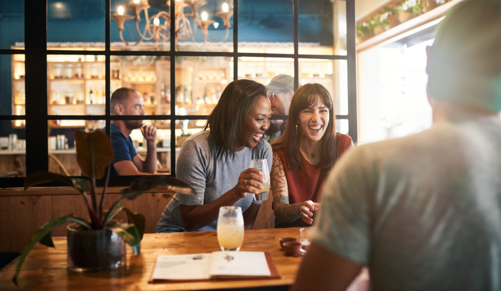Diverse group of smiling friends sitting together at a bar table laughing and talking over drinks